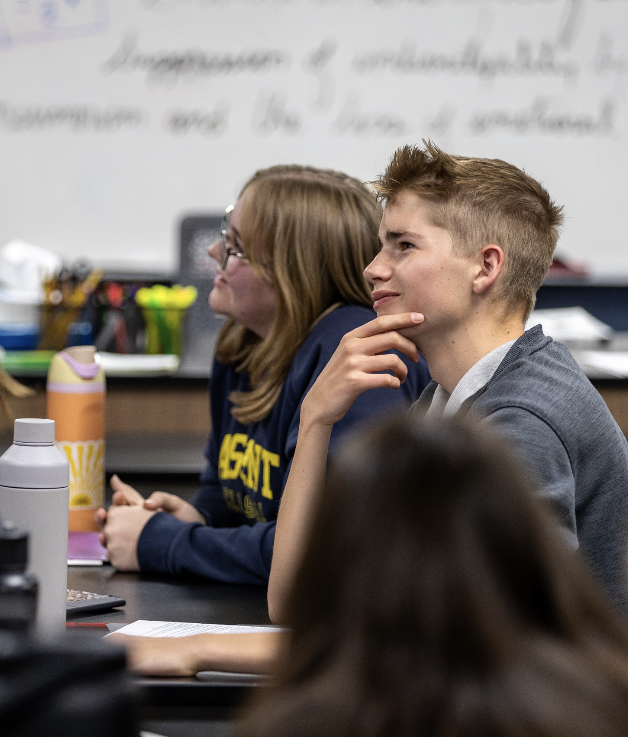Students laughing in a group, some are standing and some are sitting on a picnic table.